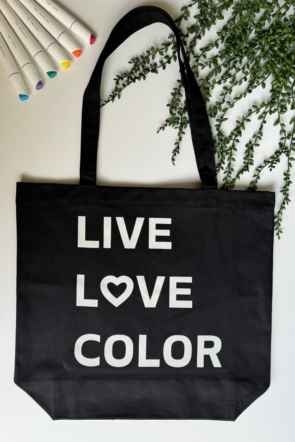 Black canvas tote bag with white bold print that says LIVE LOVE COLOR. The letter O in the word LOVE has been replaced with a heart symbol.