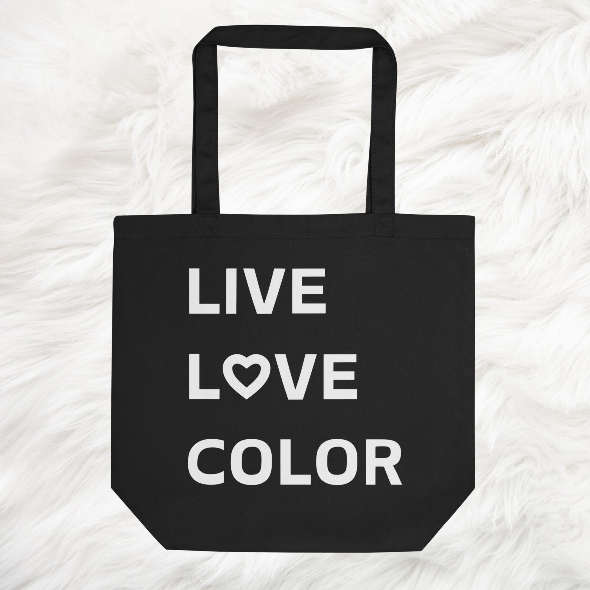 Black canvas tote bag with white bold print that says LIVE LOVE COLOR. The letter O in the word LOVE has been replaced with a heart symbol.