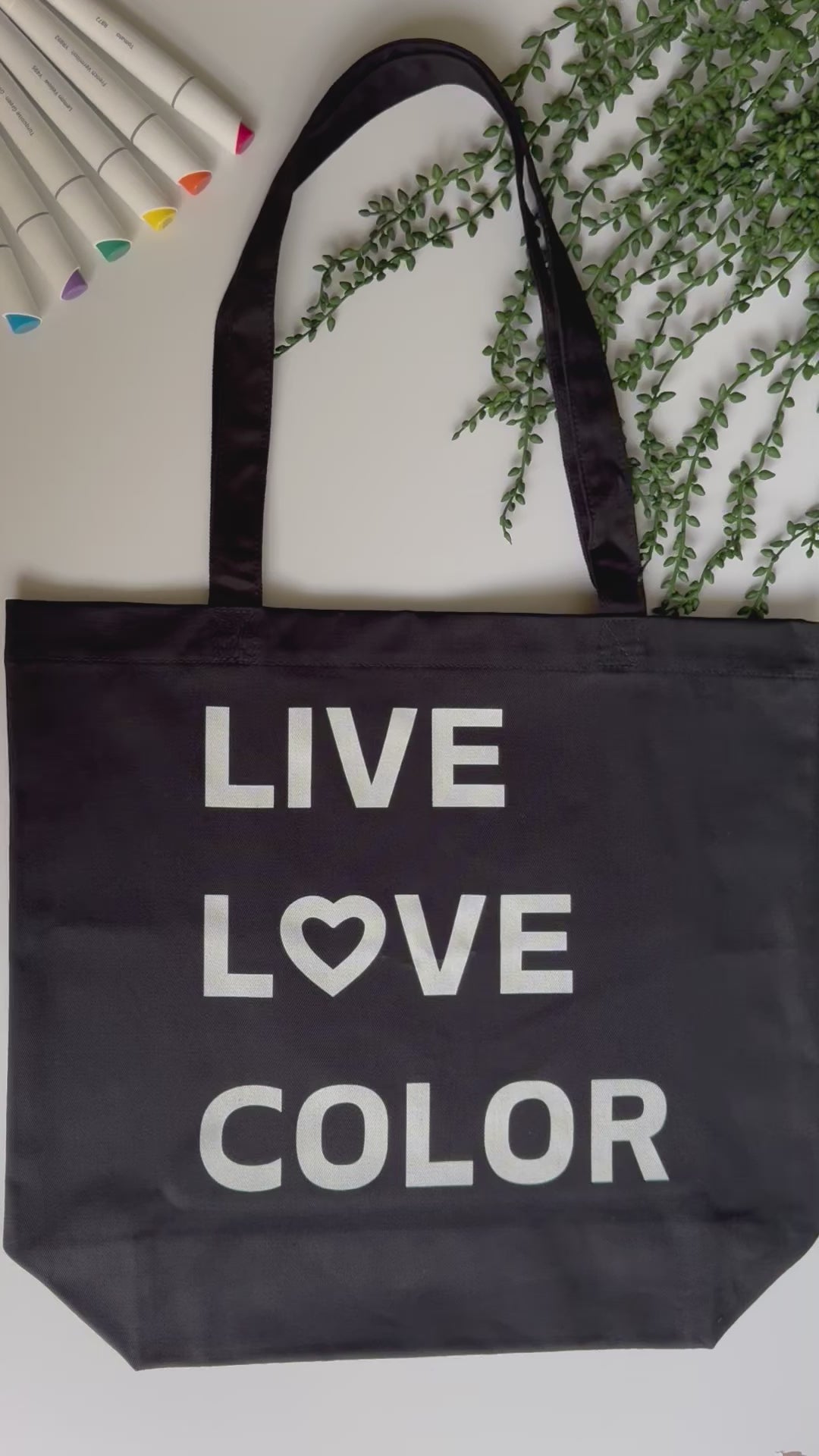 Black canvas tote bag with white bold print that says LIVE LOVE COLOR. The letter O in the word LOVE has been replaced with a heart symbol.