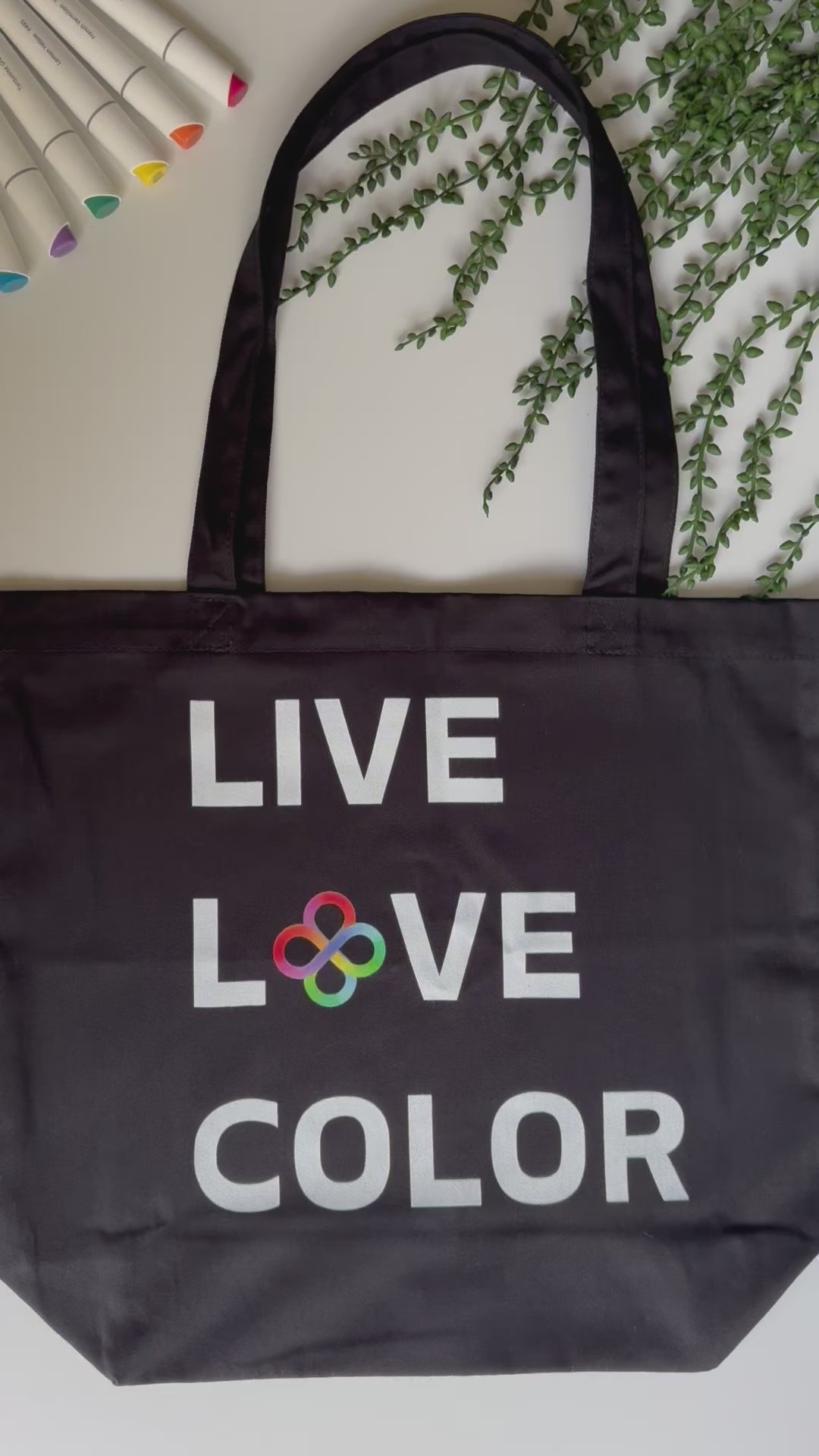 Black canvas tote bag with white bold print that says LIVE LOVE COLOR. The letter O in the word LOVE has been replaced with rainbow infinity symbols.