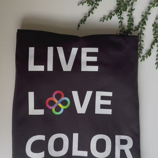 Black color tshirt with white bold print that says LIVE LOVE COLOR. The letter O in the word LOVE has been replaced with rainbow infinity symbols.