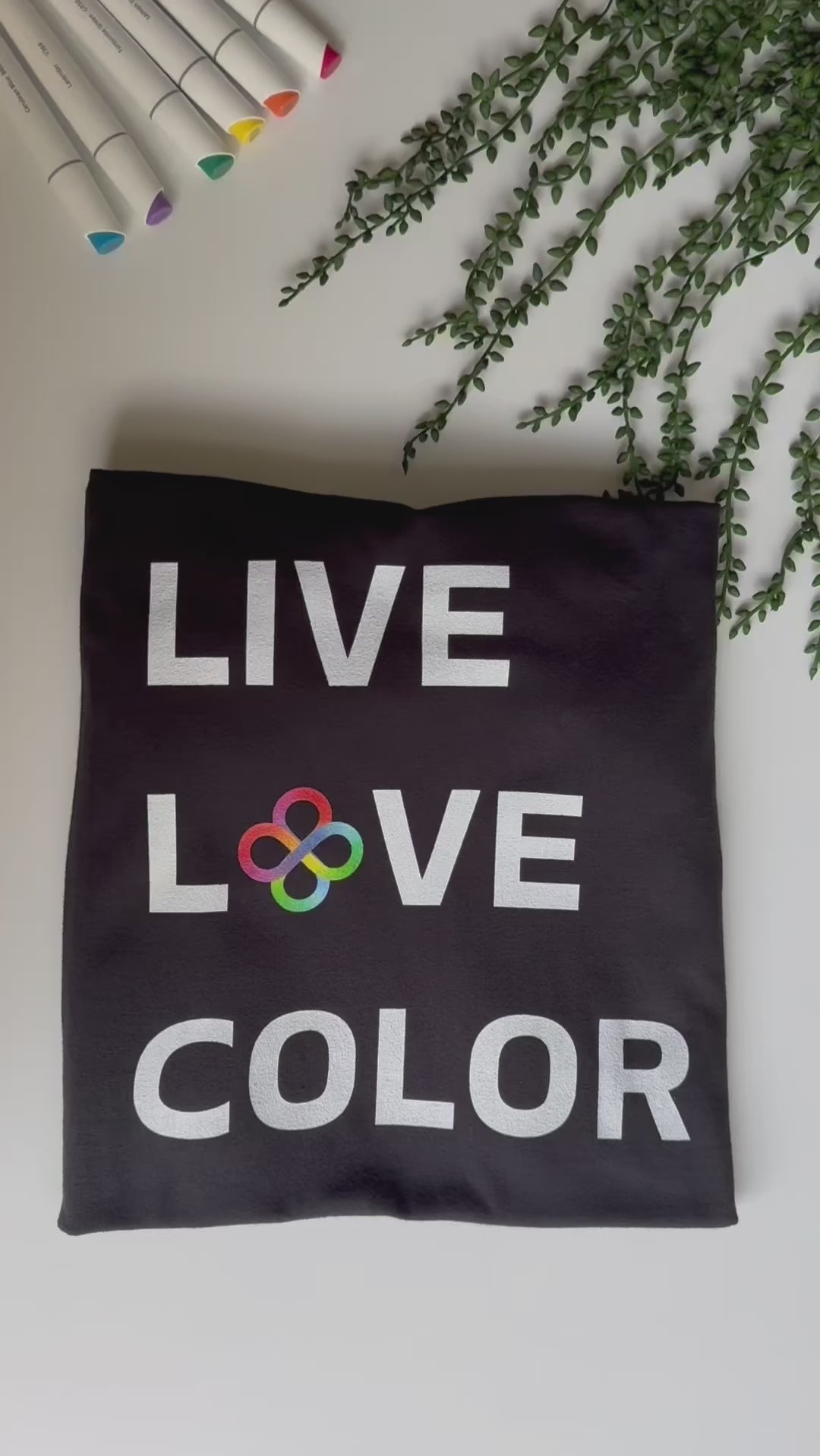 Black color tshirt with white bold print that says LIVE LOVE COLOR. The letter O in the word LOVE has been replaced with rainbow infinity symbols.